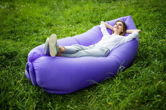 Take a break. Pretty young woman lying on inflatable sofa lamzac while resting on grass in park on the sun