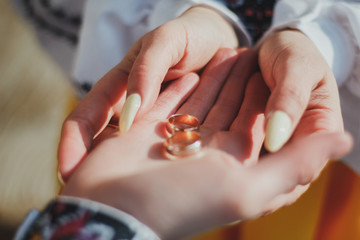 Wedding couple is holding golden rings in hands. Bride and groom are in embroidered shirts. Traditional ukrainian engagement ceremony on sunny day.