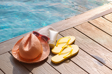 Hat, sunglasses and sunscreen at the side of swimming pool, summer travel concept