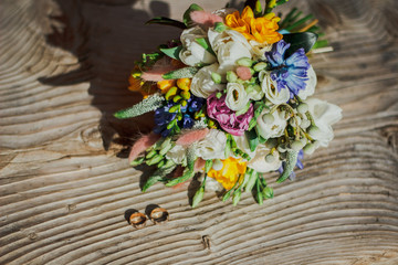 Fototapeta na wymiar Bright summer wedding bouquet is lying on the wooden bench. Sun lights on wedding decorative details.