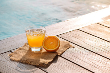 Close up of screwdriver cocktail alcohol drink with orange juice, slices and ice standing near the pool. Refreshing iced lemonade beverage in glass by the poolside. Sun glares. Background, copy space.