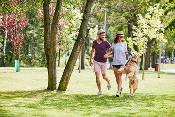 Young couple running and playing with their dog outdoors in the morning