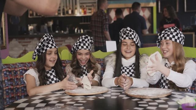 Four cheerful girls in uniform cooking a pizza on master class of chief