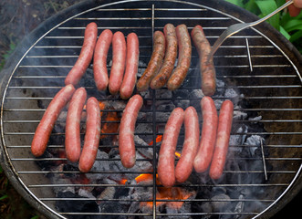BBQ-sausages grilling. Raw sausages on barbecue grill in the process of cooking. Turning with fork.