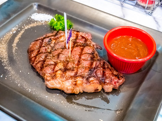 Grilled ribeye beef steak, sauce,herbs and spices on black plate. Top view with copy space for your text.