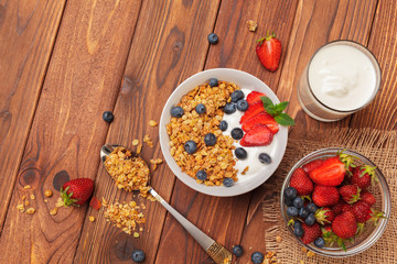 Bowl of homemade granola with yogurt and fresh berries on wooden background
