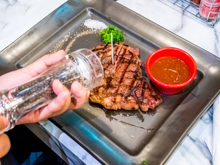 Grilled ribeye beef steak, sauce,herbs and spices on black plate. Top view with copy space for your text.