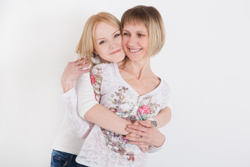 mother and her adult daughter are hugging, looking at camera and smiling

