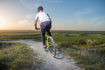 A cyclist rides a mountain bike along the trail for the evening at sunset.  Back view.