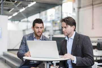 Fototapeta na wymiar Two businessmen sharing laptop in factory