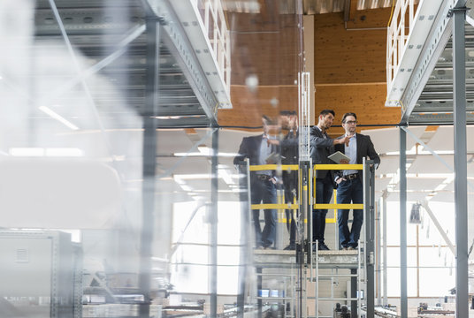 Two businessmen with tablet talking in modern factory