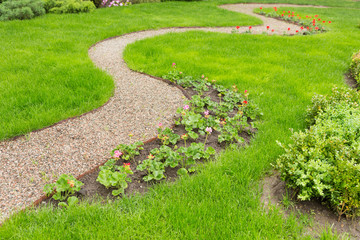 a winding footpath in the garden, a path of small gravel, green grass and flowers along the path