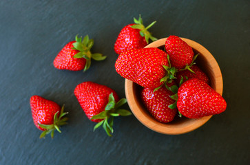 Handful of strawberry crop in a wooden plate on a cuisine background