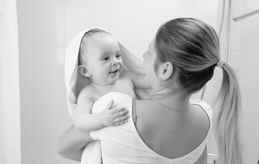 Black and white portrait of smiling baby boy covered in towel looking on mother after having bath