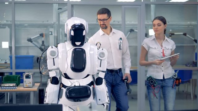 Human-like robot is getting switched on by a male engineer who is then telling something to a female one