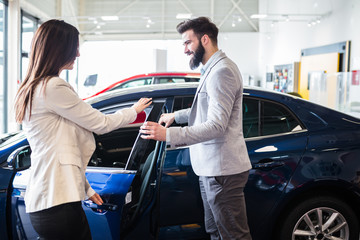 Fototapeta na wymiar Young man talking with sales woman and choosing a new car at car showroom.
