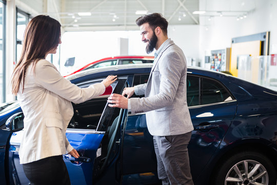 Young man talking with sales woman and choosing a new car at car showroom.