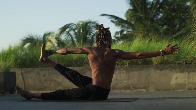Man practice spine twisting yoga pose at rooftop at sunset rapid slow motion