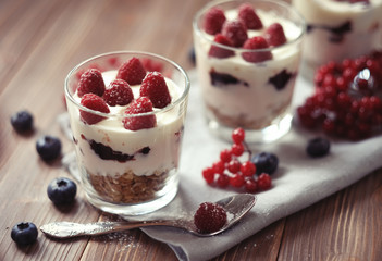 Healthy breakfast - yogurt with fresh berries and muesli served in glass jar, on wooden background