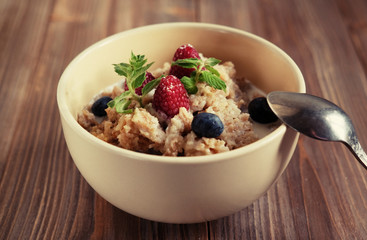 Oatmeal porridge in bowl topped with fresh blueberries and raspberries on wooden table.