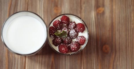 A glass of milk and granola with raspberries over wooden background, top view, close up.