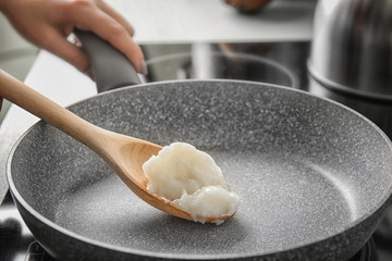Woman cooking with coconut oil in frying pan - obrazy, fototapety, plakaty