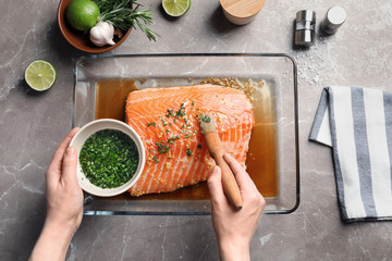 Woman marinating raw salmon in dish at table