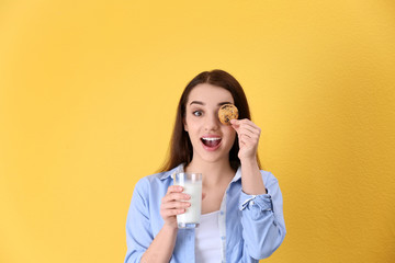 Beautiful young woman drinking milk with cookie on color background