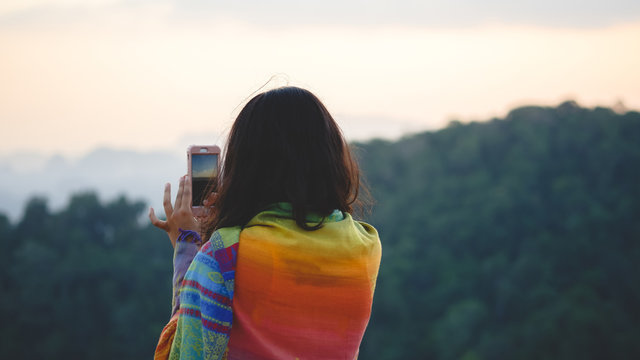 Young woman traveler taking photo with smartphone while standing at mountain.