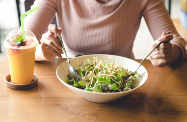 Asian woman holding fork and spoon to eating vegetable salad with orange juice at lunch in cafe.