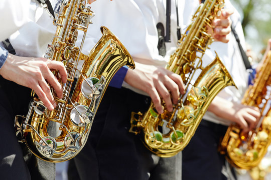 A group of young musicians in the youth brass band play on the golden saxophones.