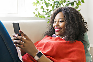 Attractive black young woman using a cellphone while relaxing on a sofa at home