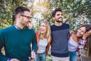 Image of four happy smiling young friends walking outdoors in the park holding digital tablet