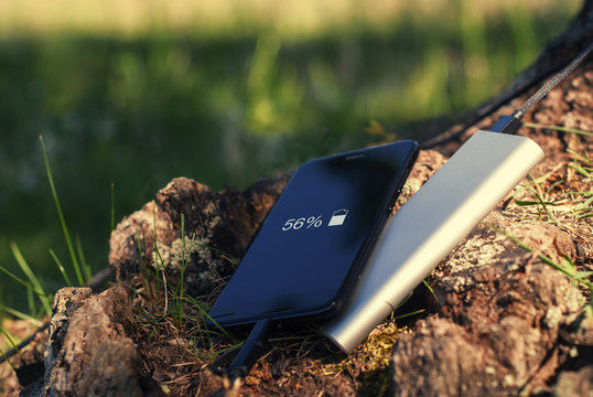 A Portable Charger Charges The Smartphone. Power Bank With Cable Against The Background Of Wood