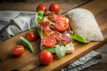 Ciabatta sandwich with arugula salad, bacon and yellow cheese.