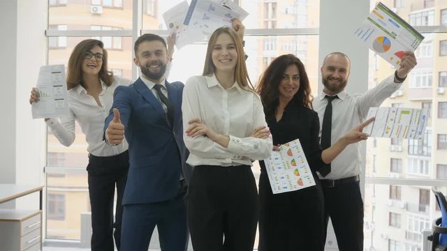 Office workers, two young men and three young women lined up in a pygmy triangle, on a pelnea plan a woman, everyone else holds office documents raise their hands up and then show class