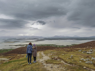 Fototapeta premium Mother and daughter taking in beautiful view from Croagh Patrick trail, Ireland county Mayo. Concept travel, memory, trip, adventure.