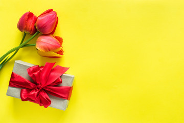 Gift box with red ribbon bow flower Bouquet tulips on bright yellow background Copy space for text