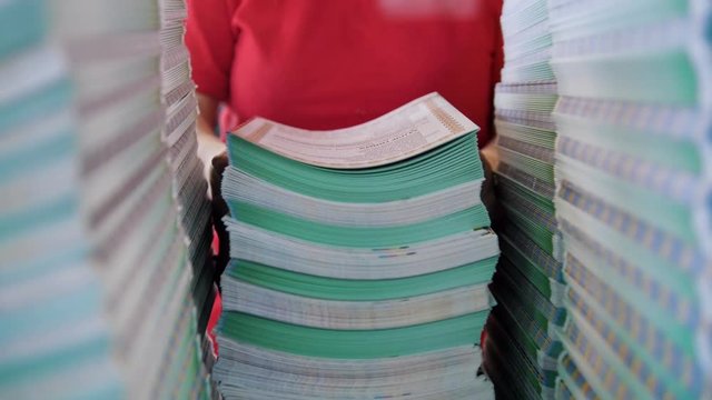 Female worker lays out a large stacks of paper from the box in the typography