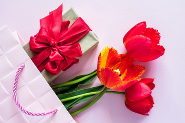 Gift box with red ribbon bouquet of tulips in Pink package on delicate pastel background