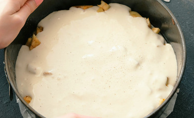Close-up woman's hands put the batter with the Apple slices in a baking sheet covered with parchment. Cooking apple pie.