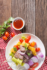 Bbq meat on sticks, kebab skewers with vegetable sticks and tomato sauce on wooden background.