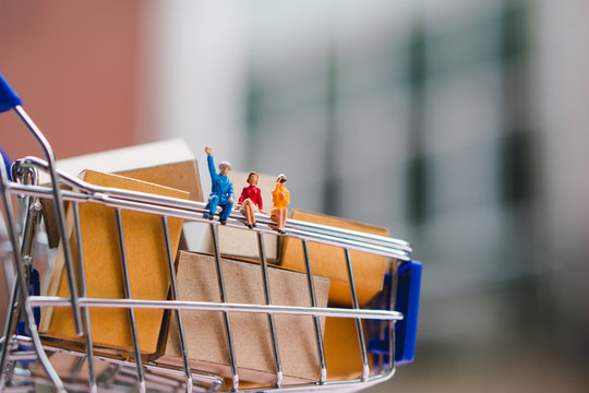 Miniature man and woman sitting on shopping cart contain paper box using as e-commerce, online shopping concept