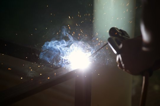 Worker is welding sparks table steel in factory.