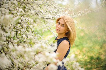 Beautiful girl standing between branches of white blossom tree