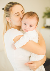 Portrait of happy young woman hugging and kissing her cute baby