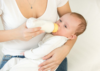 Obraz na płótnie Canvas Portrait of 3 months old baby boy drinking milk from bottle on mothers lap