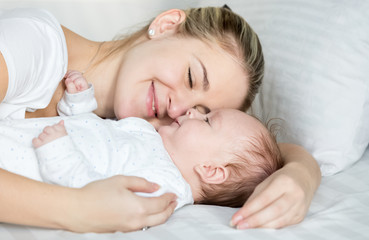 Portrait of beautiful smiling woman lying with her baby on bed