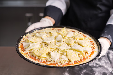 Chef making pizza with cheese at kitchen.