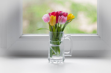 piccoli tulipani colorati su una finestra bianca in una tazza di vetro